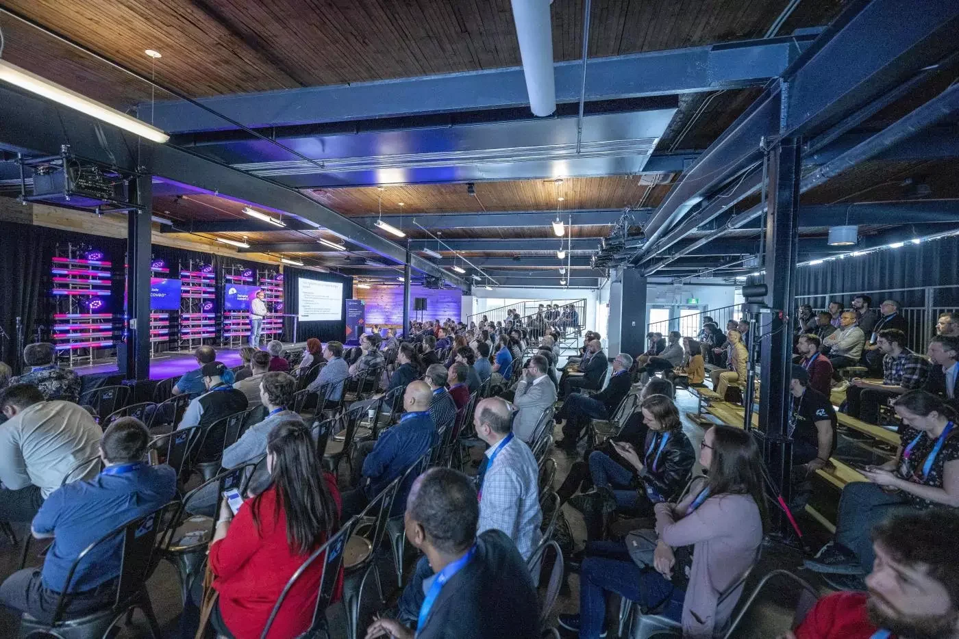 Conférence avec public assis écoutant un présentateur sur scène.